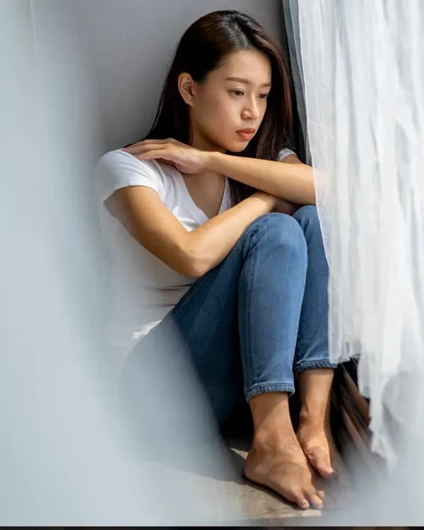 Woman seated against a wall, hands resting on knees