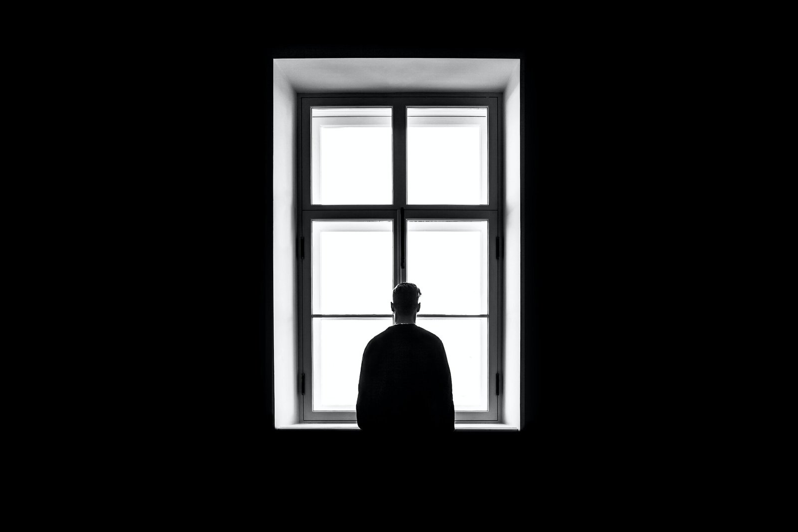 a black and white image of someone staring out a window in a dark room