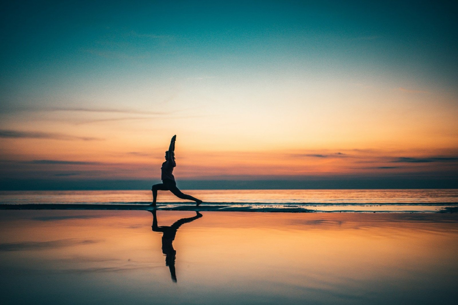 Someone doing yoga on a beach with the sunset in the background