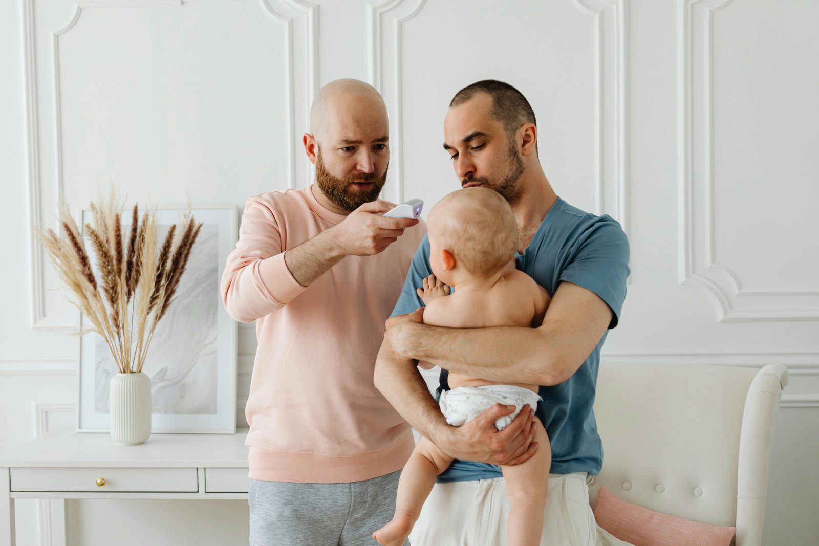 Free A worried father checks baby's temperature while partner holds the child at home. Stock Photo